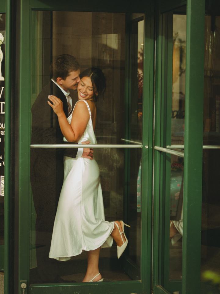 Couple embracing inside a green revolving door, her heel lifted