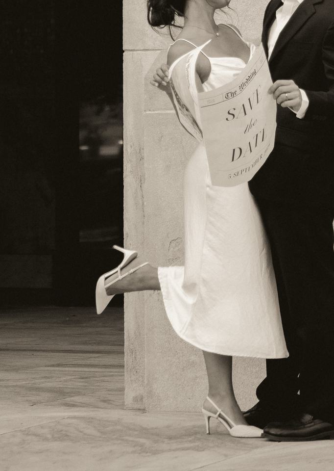 Black-and-white couple, she kicks up a heel holding a save-the-date